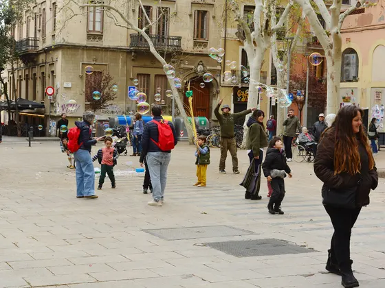 La plaza de la Virreina con su suelo de losas, árboles sin hojas, edificios de tres y cuatro plantas al fondo y gente cruzando y charlando en la plaza.