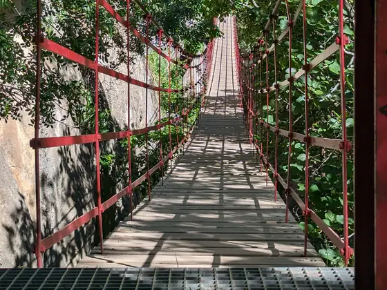 Puente colgante de tablas y cables sobre el desfiladero del río Monachil, entre paredes de roca y vegetación.