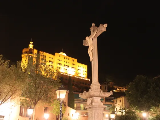 El Cristo de los Favores de noche en el Campo del Príncipe, con el hotel Alhambra Palace iluminado en la colina de detrás.