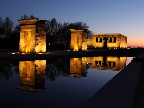 El Templo de Debod iluminado al anochecer, con las dos puertas de piedra y el templo reflejados enteros en el estanque.