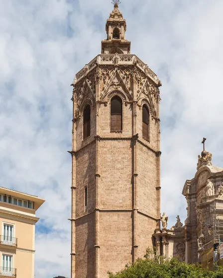 El Micalet, la torre octogonal de piedra de la Catedral, visto desde abajo, con el remate del campanario arriba y nubes blancas detrás.